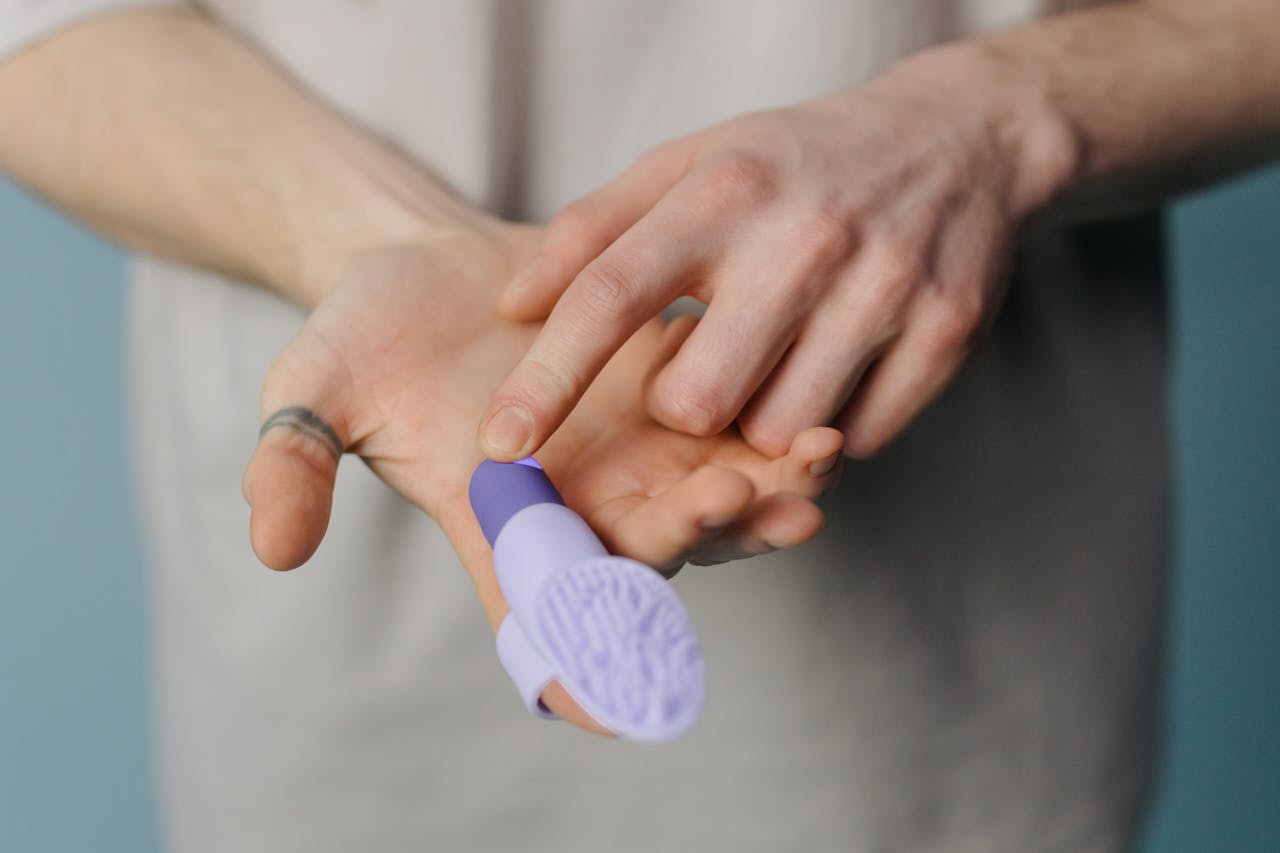 home-hero An adult hand holding a purple silicone finger massager against a neutral background.